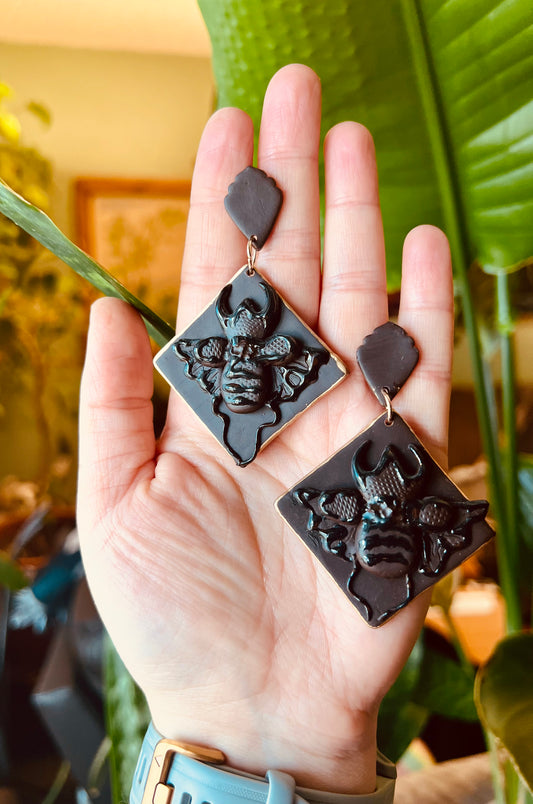 Tap into the strength and transformative properties of with our polymer clay stag beetle earrings, featuring a monochrome dark brown hue and elegant gold trim. Available now! They make the perfect unique gift for nature lovers, and gothic chic enthusiasts.