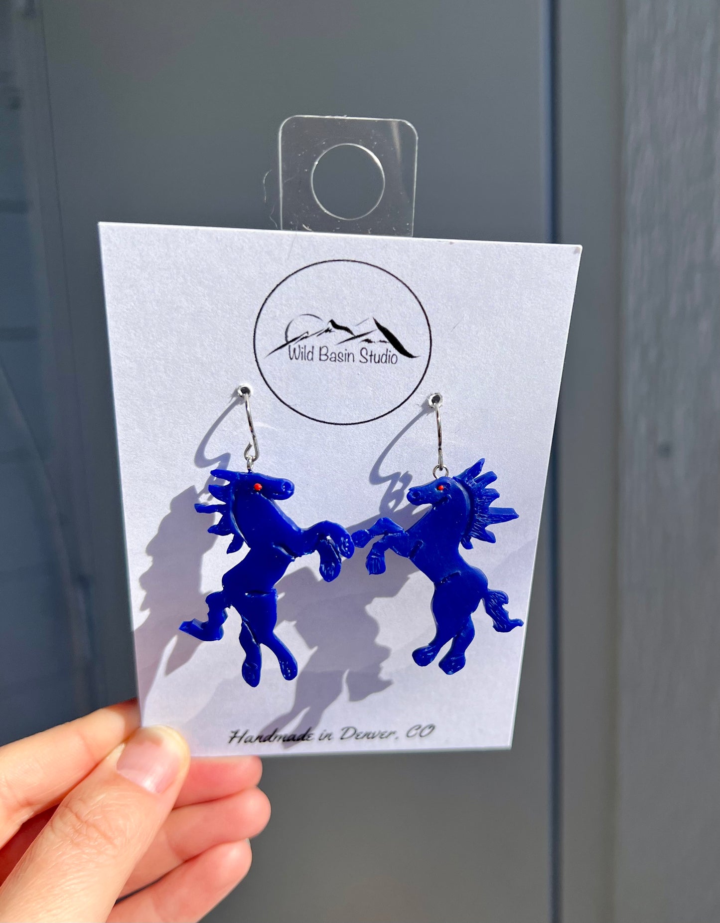 Capture the intrigue of Denver's infamous Blue Mustang sculpture with our polymer clay earrings featuring Blucifer and his piercing red eyes. These unique earrings pay homage to the iconic landmark at DIA, adding a bold and unforgettable touch to your style. Channel the spirit of the Mile High City with these statement pieces!