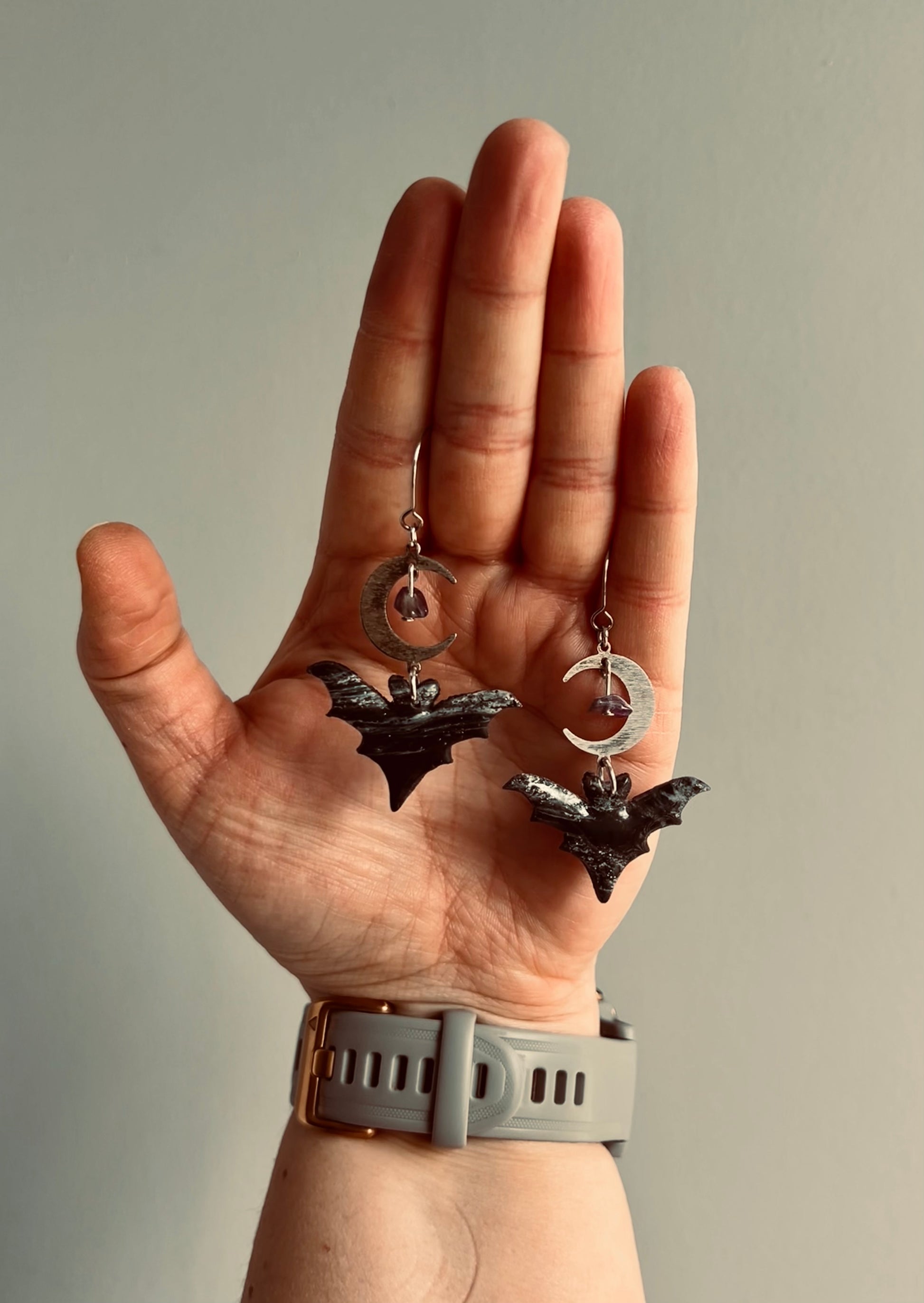 Embrace the mystical allure of our bat earrings, adorned with a moon charm and shimmering amethysts, evoking the magic of lunar cycles and inner peace.