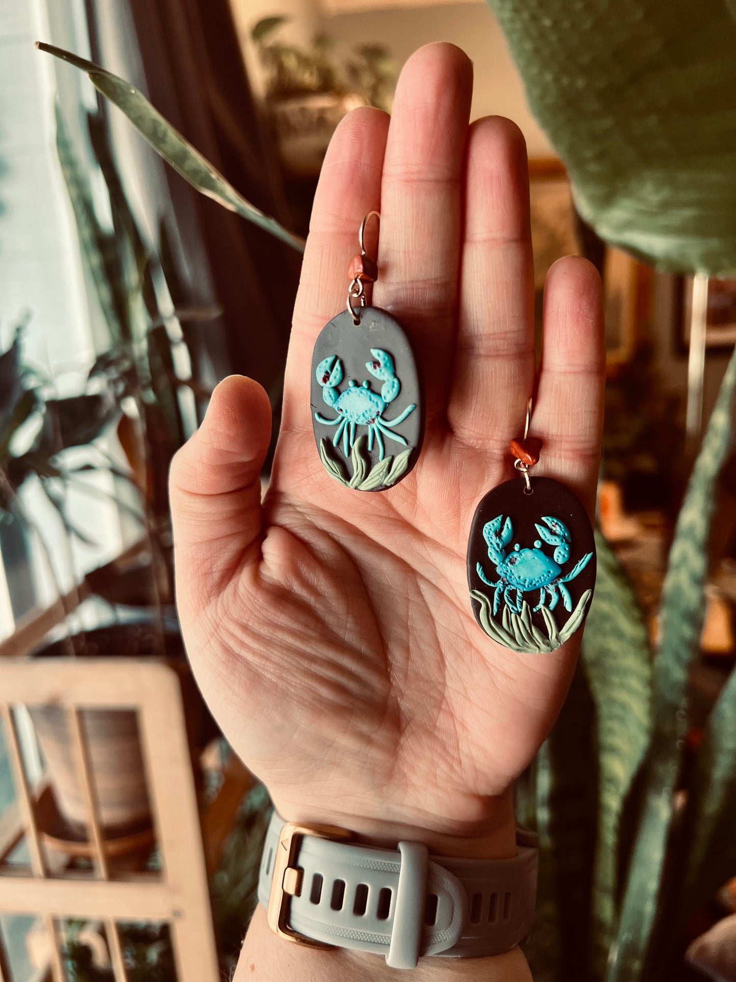 Intricate polymer clay Cancer earrings, meticulously hand-sculpted using Sculpey clay. Embrace the nurturing essence of the Cancer zodiac sign with these artisanal earrings, symbolizing emotional depth and intuitive energy.  These earrings depict a blue crab in the depths of the ocean entangled in seaweed.