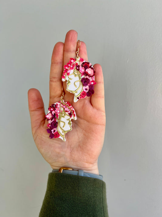 Elevate your accessory game with our stunning polymer clay earrings featuring a graceful woman adorned with a bouquet of pink flowers in her hair. Each delicate petal showcases a unique shade of pink, adding a touch of feminine elegance to any ensemble. Embrace the beauty of nature with these intricately crafted statement earrings.