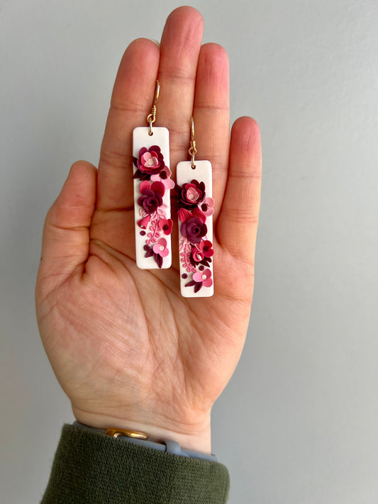 Adorn yourself with the delicate beauty of polymer clay earrings featuring a white background and an array of pink-hued flowers. Each petal bursts with elegance and charm, creating a captivating accessory for any occasion. Embrace the floral fantasy and add a touch of whimsy to your look today!