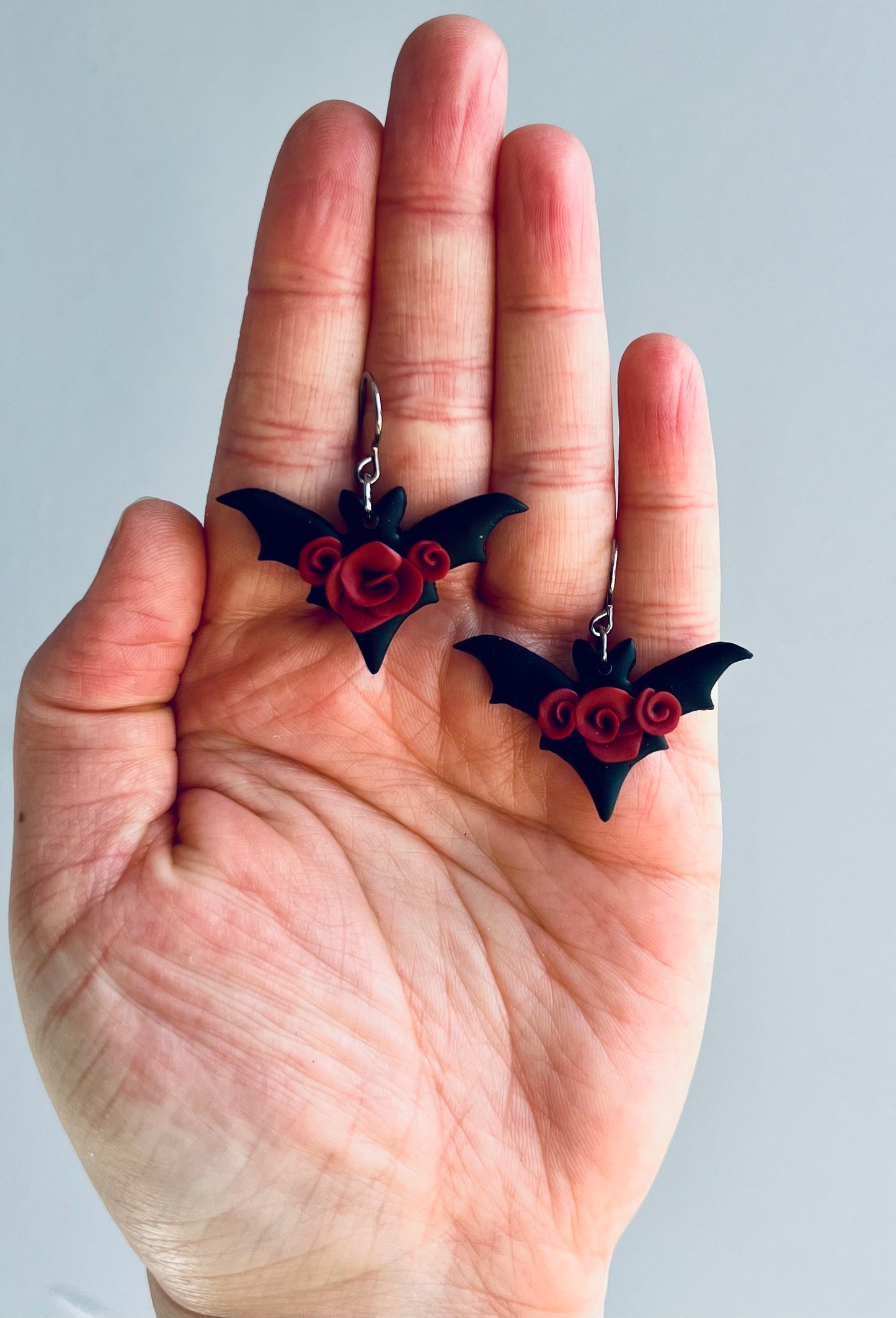Captivating black bat earrings adorned with striking red roses, evoking an aura of dark romance and gothic elegance.
