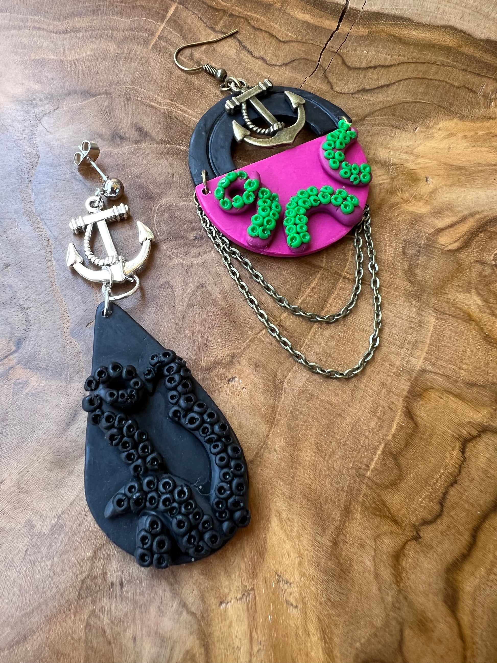 Side by side comparison of black kraken earrings, and fuchsia kraken polymer clay earrings. Each pair is adorned with an anchor to ensure stability, strength, and security, serving as a reminder to stay grounded amidst life's turbulent waters.